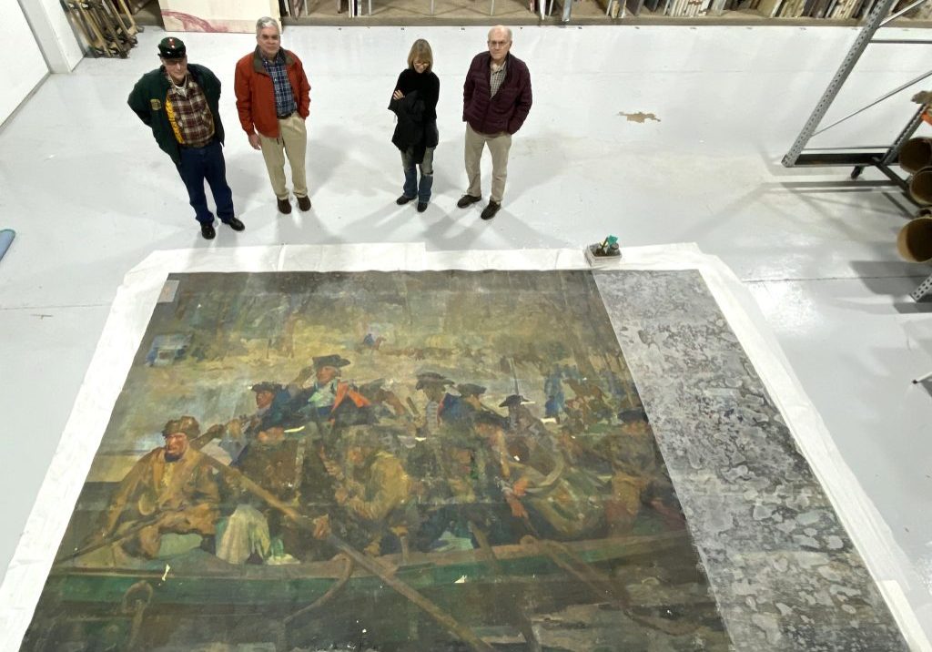 Four people standing at the top of a large mural of Washington crossing the Delaware, which is flat on the floor.